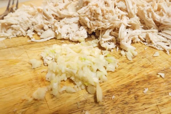 Shredded chicken and chopped garlic on wooden cutting board for the Authentic Mexican Chicken Enchiladas with Red Sauce.
