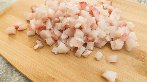 Tilapia cut into small cubes for Tilapia Ceviche on a wooden cutting board.