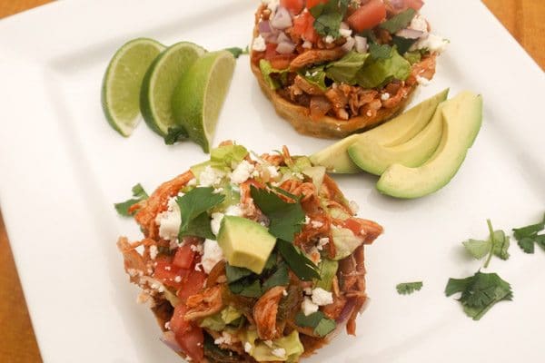 Chicken Sopes with all the toppings! Avocado, queso fresco, tomatoes, onions, salsa verde and red sauce served on a white platter.