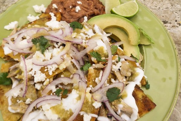 Chilaquiles Verdes with Chicken made with corn tortillas, shredded chicken, salsa verde, topped with queso fresco, mexican crema, thinly sliced red onions and served with refried beans and avocado slices.