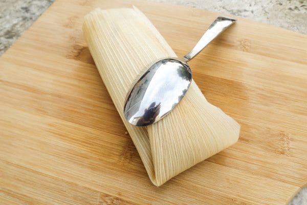 Fully folded tamale on top of a wooden cutting board-Beef Mexican Tamales