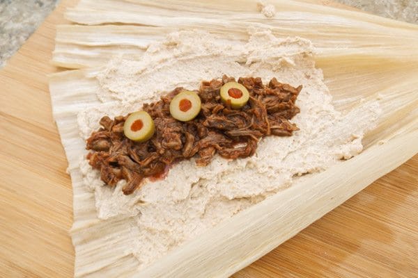 Savory beef added to masa dough on corn husk with olives on top of beef-Beef Mexican Tamales