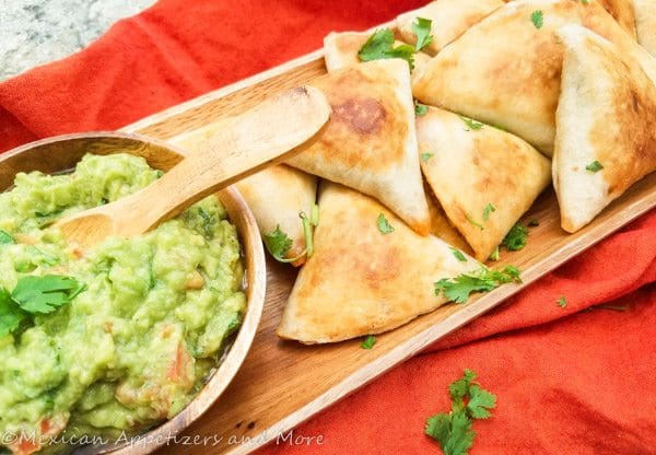 Mexican Samosas aerved on a wooden platter with guacamole.