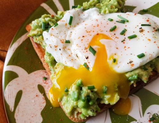This simple poached egg and avocado toast is made with avocado spread that includes chives and cayenne pepper with a poached egg on toast served on a green and white plate.