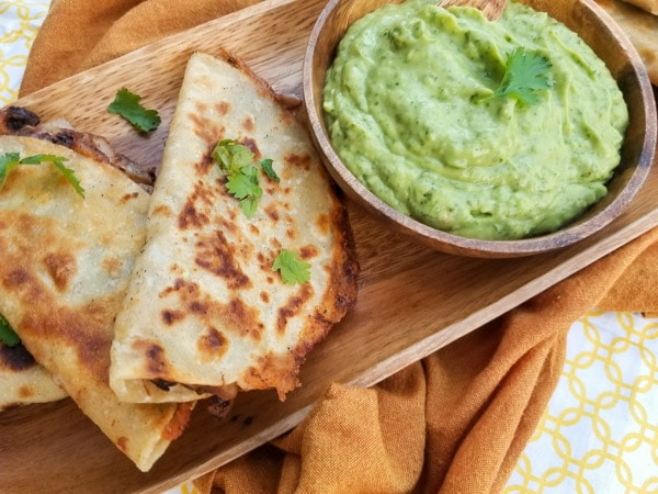 Crispy Black Bean Tacos made with black beans, tomato sauce, red onions, garlic. jalapeno, smoky spices, pepper jack cheese, wrapped in a crispy corn tortilla and served with avocado cilantro sauce served on a wooden platter.