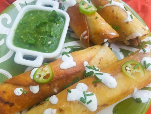 Chicken Poblano Flautas served with salsa verde on a green platter.