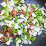 Sauteing the peppers and onions with the bacon pieces in a skillet for the Arroz Mamposteao