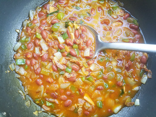 Beans are added to the peppers, onions, bacon and garlic to skillet.