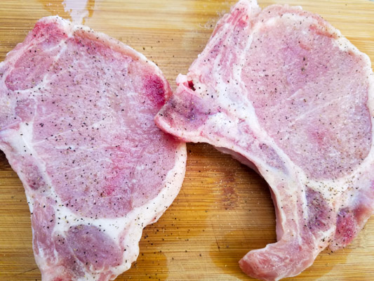 Raw seasoned pork chops on a cutting board for the chuletas de puerco recipe (pork chops in salsa verde)