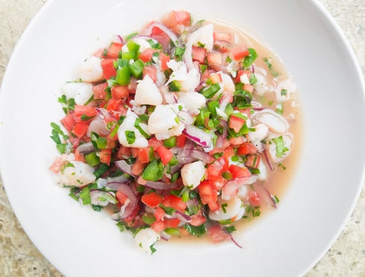 Shrimp ceviche prepared with red onions, tomatoes, jalapeño, garlic and cilantro in a white bowl.