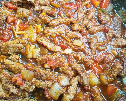 Bistec a la Mexicana (Steak a la Mexicana) cooking in a savory tomato chile sauce in a skillet.