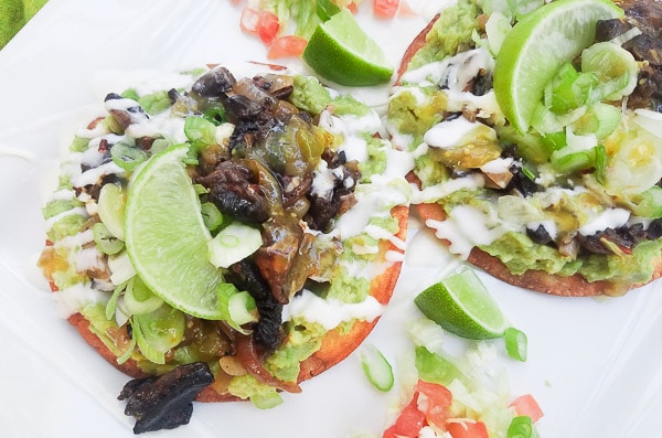 Avocado and Chipotle Mushroom Tostadas served on a white platter and topped with lime wedges.