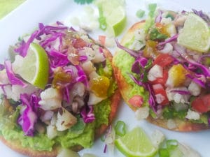 Cauliflower Ceviche Tostadas with guacamole. shredded red cabbage and salsa verde served on a white platter.