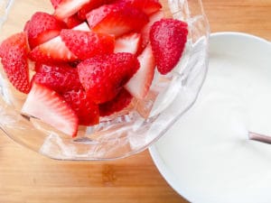 Cream prepared in a white bowl and strawberries rinsed, stemmed and cut into bite size pieces for the fresas con crema (strawberries and cream) dessert.