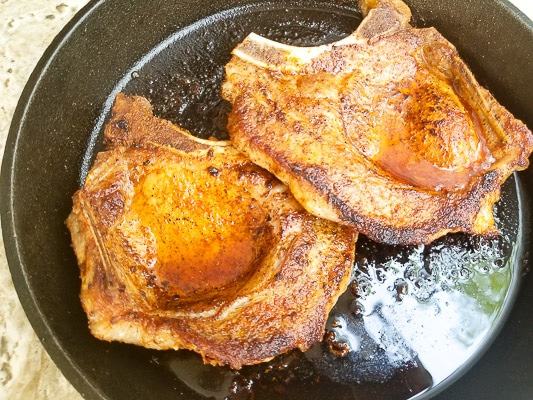 Seared pork chops in a cast iron skillet ready to finish cooking in the oven.