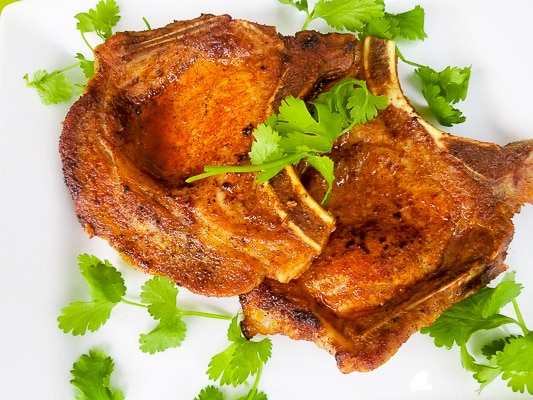 Baked pork chops served on a large white platter and topped with cilantro sprigs.