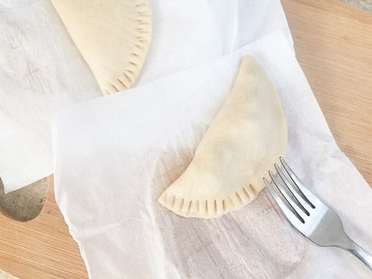 Stuffed and formed empanadillas on a cutting board. Crimping the edges with a fork.-Masa Para Empanadillas (Dough for Empanadillas)