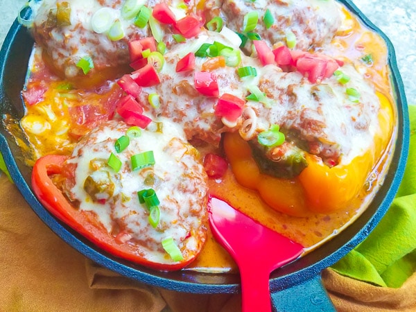 Cooked Puerto Rican Stuffed Peppers in a cast iron skillet, topped with a salsa criolla, monterey jack cheese, chopped scallions and tomatoes.