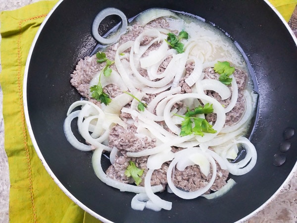 Delicious Bistec Encebollado cooked in a black skillet, loaded with white onions on top.