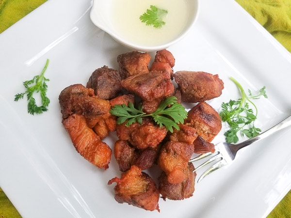 Delicious Carne Frita (Fried Pork Chunks) served with a side of garlic sauce on a white platter.