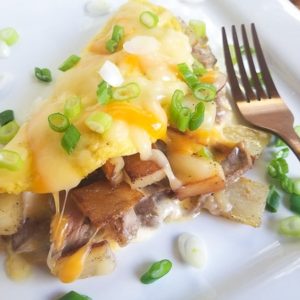 Steak Omelette with Potatoes topped with cheese and scallions. Served on a white platter.