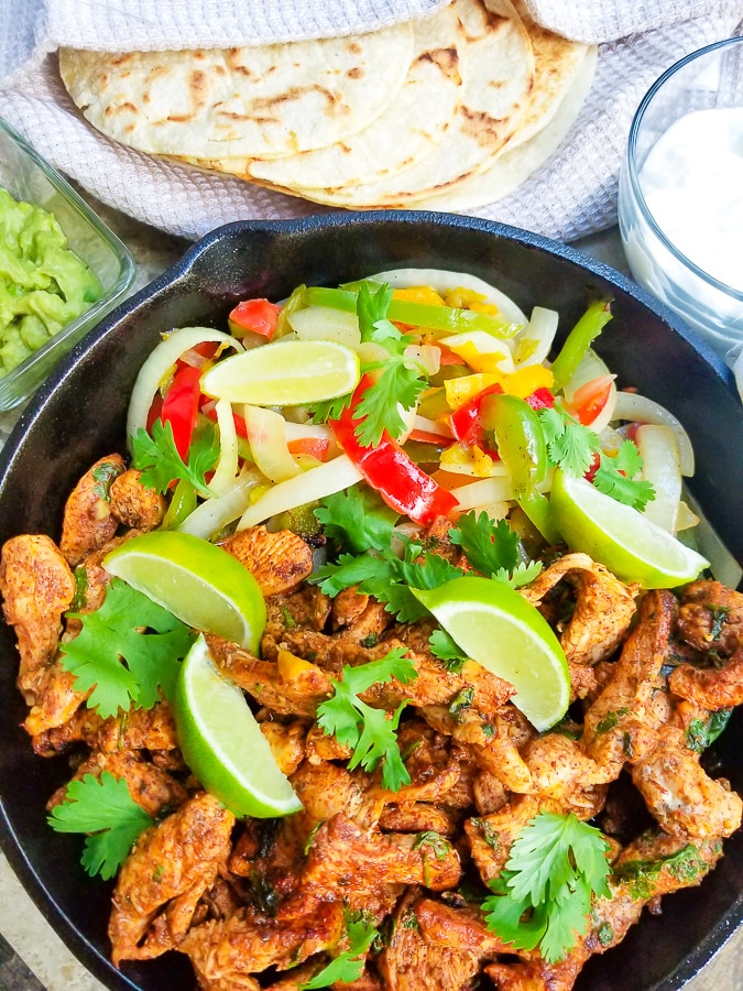 Fajitas de Pollo served with colored peppers and onions served in a skillet with a side of tortillas, guacamole and sour cream.