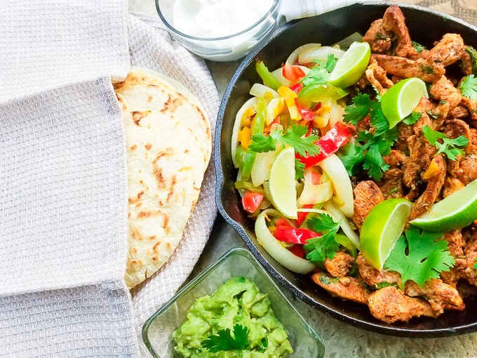 Fajitas de Pollo served with colored peppers and onions served in a skillet with a side of tortillas, guacamole and sour cream.