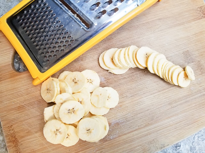 Plantain cut into thin slices using a mandelin on wooden cutting board.