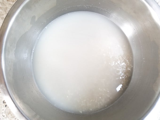 Rinsing medium grain rice of talc powder coating in bowl. Water is cloudy because of talc coating.