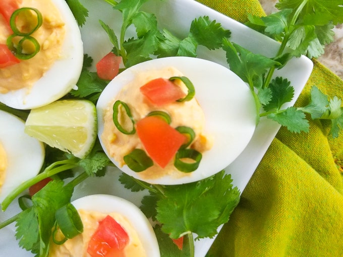 Chipotle Deviled Eggs on a white platter topped with chopped scallions and tomatoes.