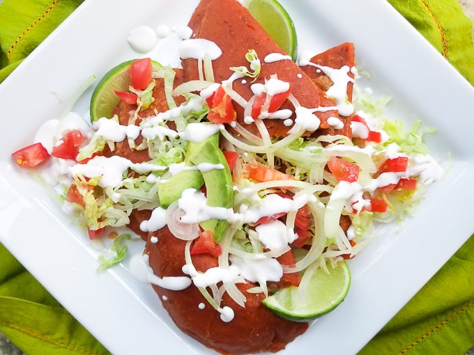 Enchiladas Potosinas served and topped with shredded lettuce, avocados, tomatoes and Mexican cream on a white platter.