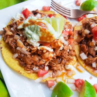 BBQ Chicken Tostadas topped with avocado/sour cream, chopped tomatoes, chopped onions and lime wedges.