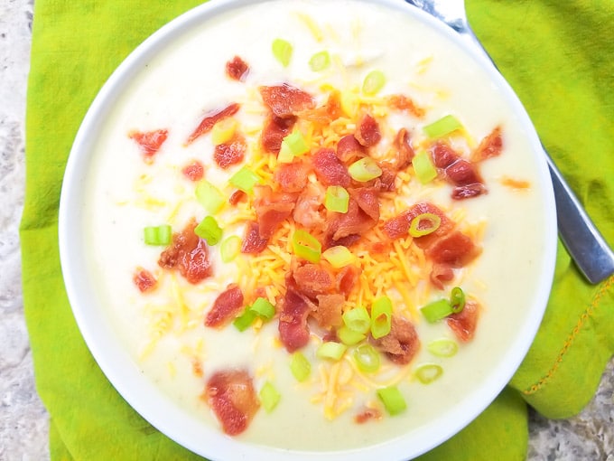 Sopa de Papa (Potato Soup) topped with bacon pieces, shredded cheddar cheese and scallions, served in a white bowl.