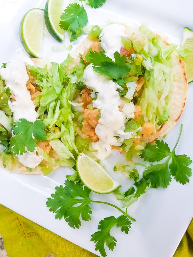 Tostadas de Camaron topped with shredded lettuce, jalapeno tartar sauce, tomatillo pico de gallo and cilantro, served on a white platter with lime wedges. 