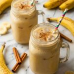 Agua de platano (banana water) served in glass mason jars with a festive Mexican straw and ripe bananas beside it.
