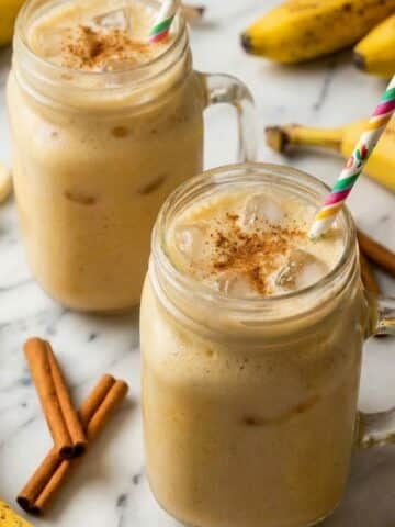 Agua de platano (banana water) served in glass mason jars with a festive Mexican straw and ripe bananas beside it.