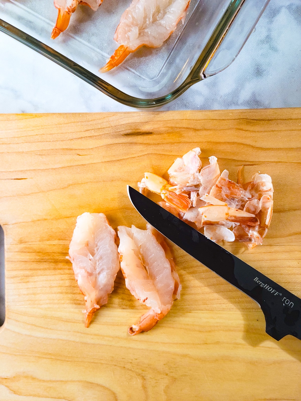 Shrimps being butterflied on a wooden cutting board.