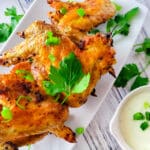 Alas de Pollo al Horno (Alitas-Baked Chicken Wings) served on a white platter with a side of ranch and barbecue sauce.