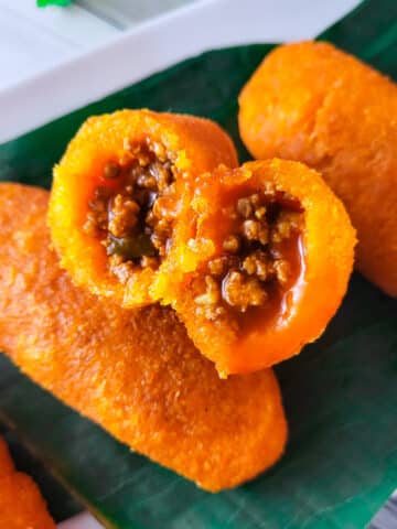 Alcapurrias de Yuca (Cassava Fritters) sitting on top of plantain leaves with a side of hot sauce.