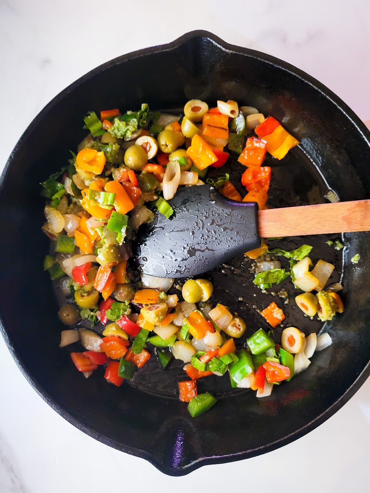 Peppers, onions, garlic, sofrito and olives sauteing in a cast iron skillet.