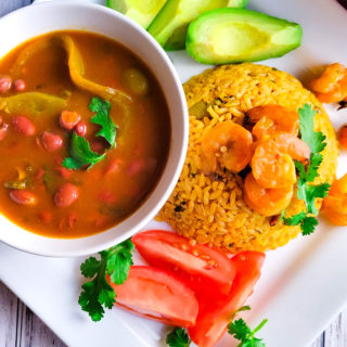 Arroz con Camarones (Puerto Rican Rice and Shrimps)served on a white plate with a side of habichuelas guisadas (puerto Rican Stewed Beans), avocado slices, and tomatoes slices.