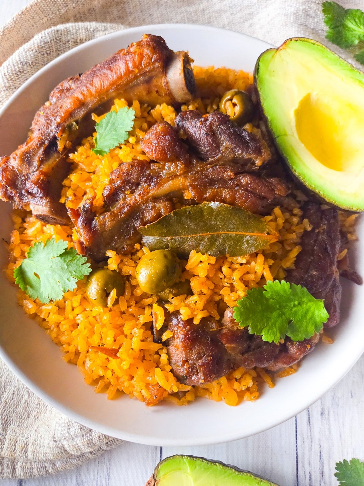 Puerto Rican arroz con costillas served on a white bowl with a side of habichuelas guisadas and avocado.
