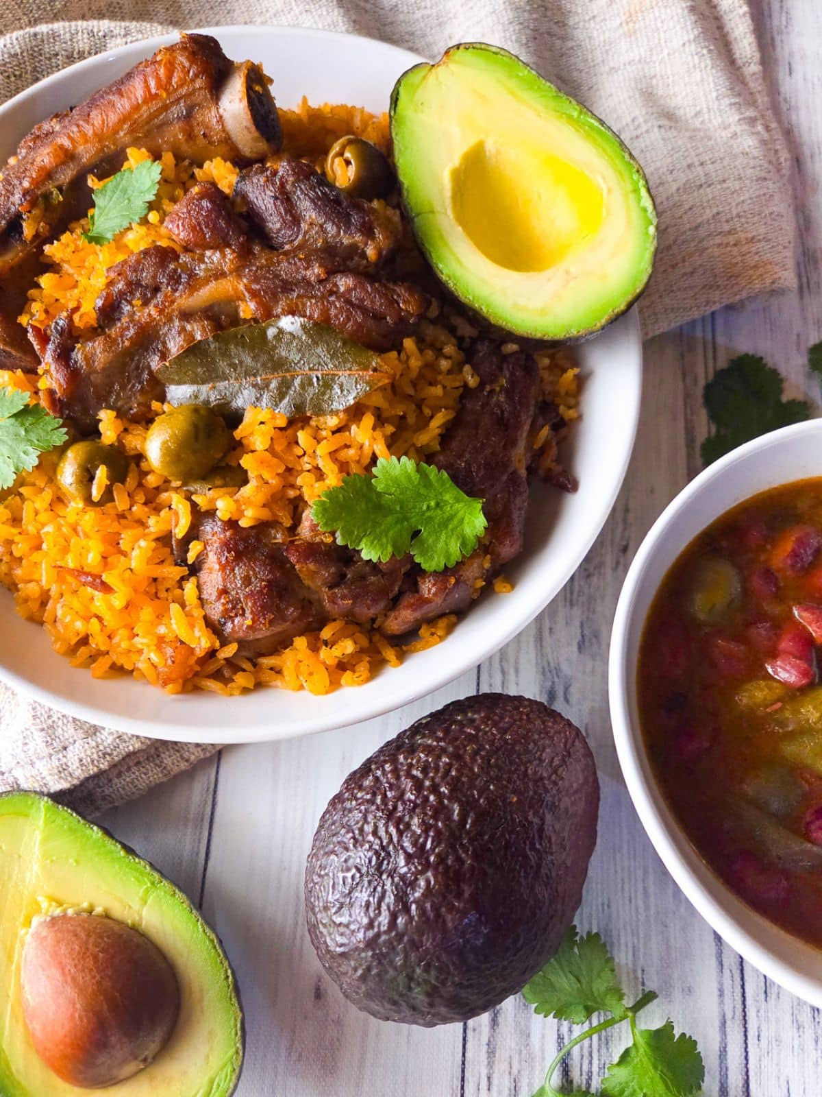 Puerto Rican arroz con costillas served on a white bowl with a side of habichuelas guisadas and avocado.