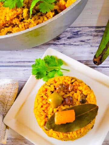 Arroz con Gandules Apastelado cooked in a caldero with a side serving on a white plate.