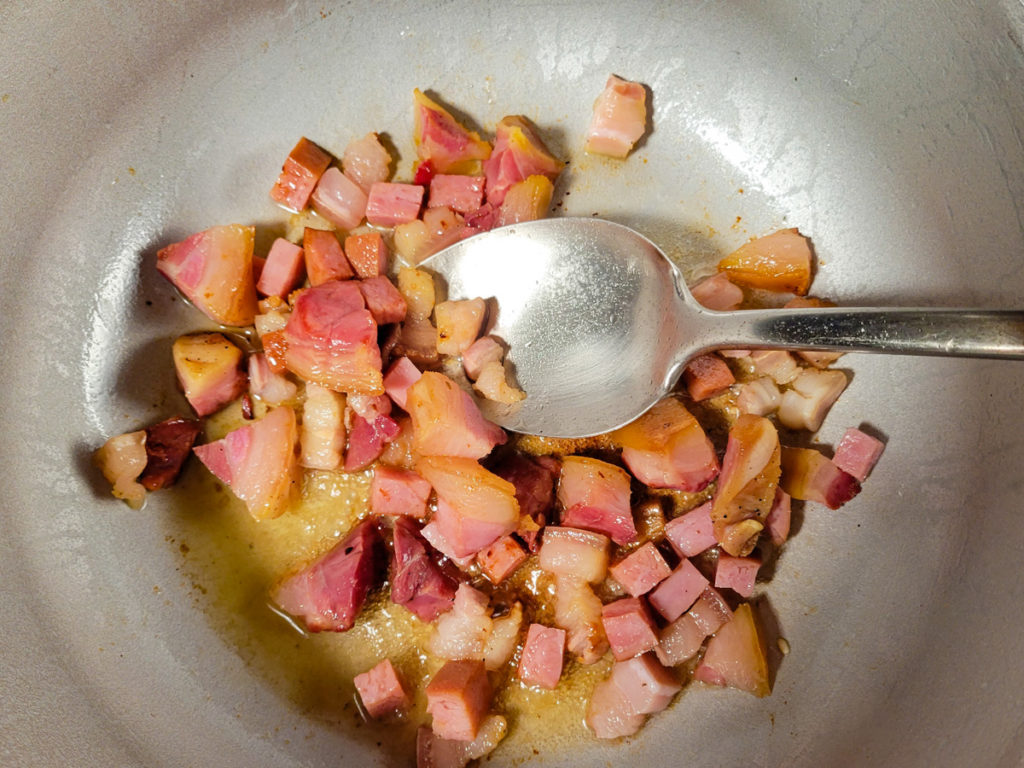 Browning the ham, tocino and hamhock pieces in the caldero for the rice apastelado.