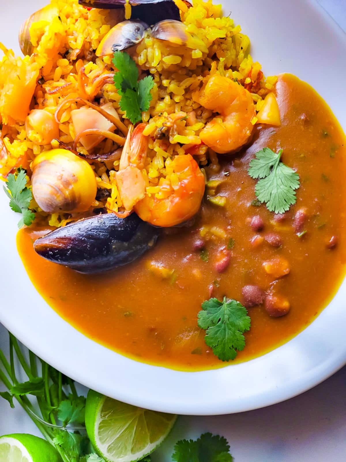Arroz con Mariscos (Puerto Rican Style Seafood Rice) served in a white plate with a side of habichuelas guisadas (stewed beans).