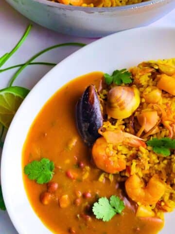 Arroz con Mariscos (Puerto Rican Style Seafood Rice served in a white plate with a side of habichuelas guisadas (stewed beans).