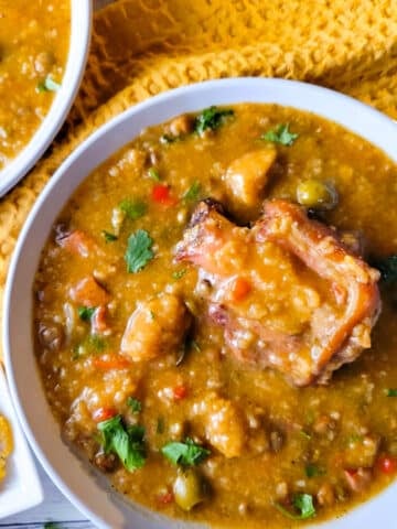 Asopao de Gandules (Pigeon Pea Stew) served in two white bowls with a side of tostones.