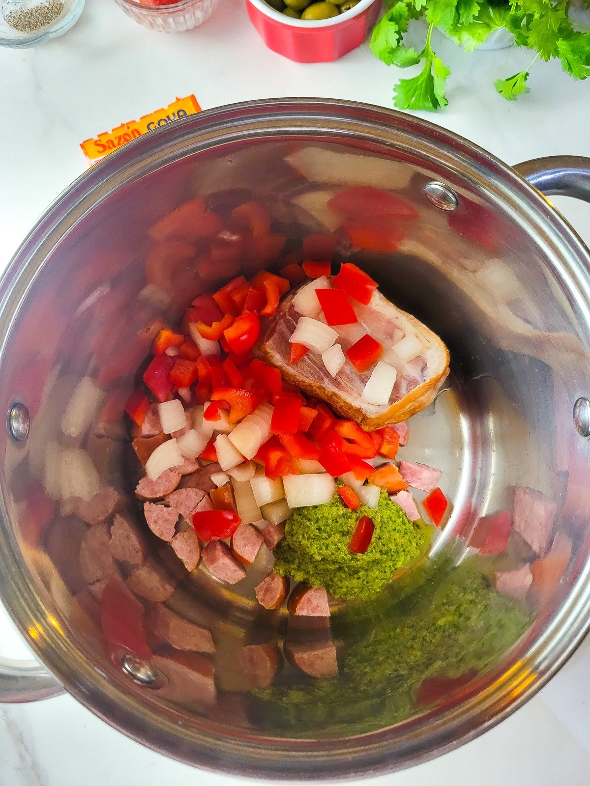 A medium size pot with the oil, ham, ham hock, sofrito, pepper and onions sauteing to form the base for asopao.