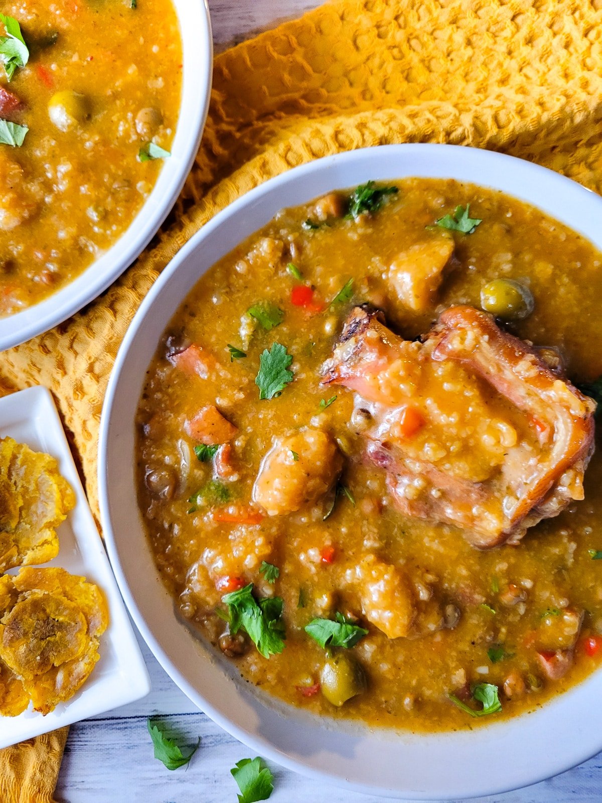 Asopao de Gandules (Pigeon Pea Stew) served in two white bowls with a side of tostones.